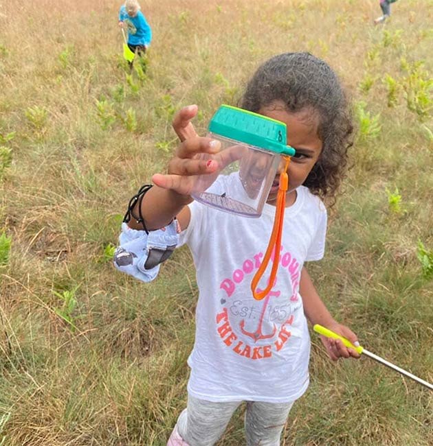 A girl showing off a bug she caught in a jar.