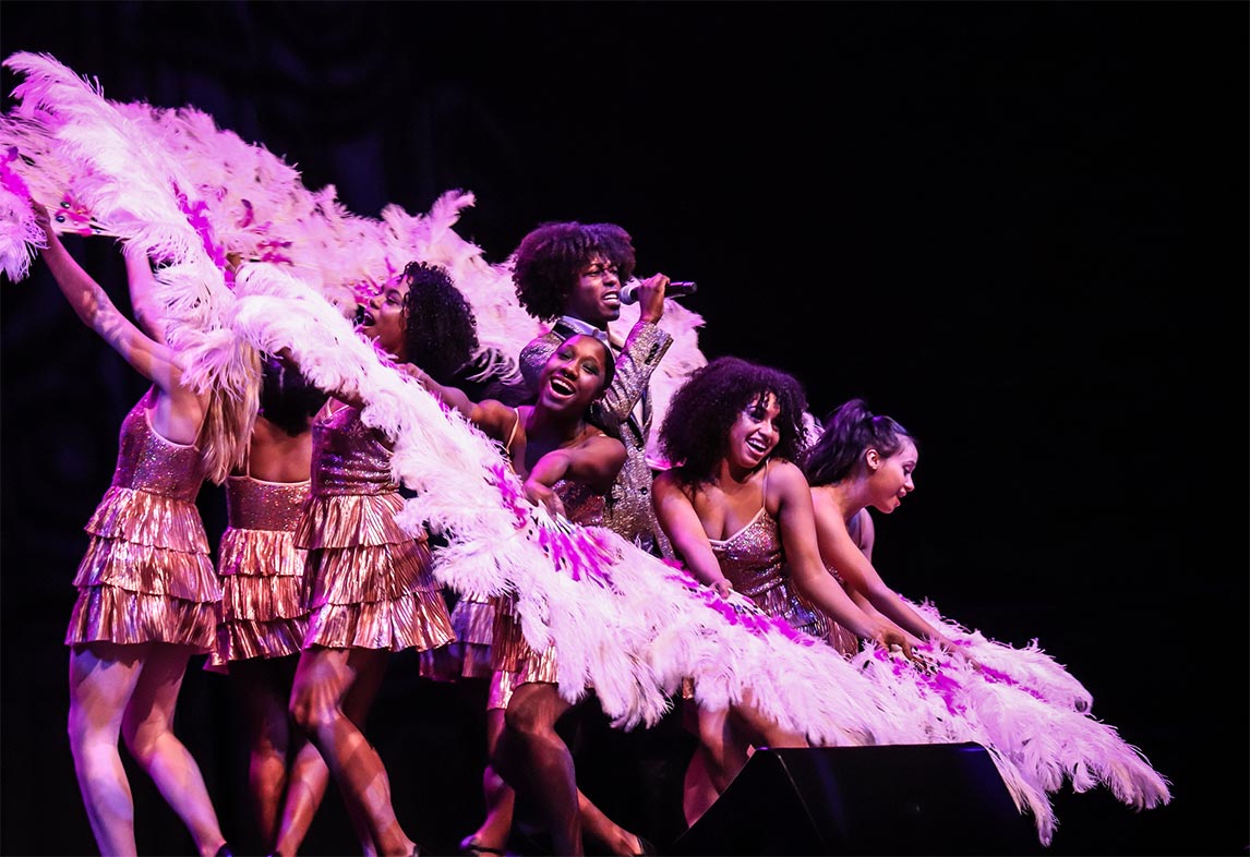 A group of ChiArts dancers surround a singer with feathered fans.